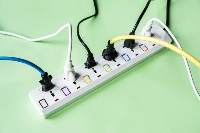 A White Power Strip With Multiple Colored Plugs Connected And A Green Background.