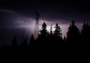 Home Service Blogs | Grand Bay Electrical Silhouetted Trees And A Power Line Tower Against A Dark Sky Illuminated By Lightning.