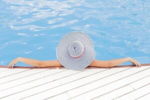 Home Service Blogs | Grand Bay Electrical Person With A Large Striped Hat Relaxing At The Edge Of A Swimming Pool, Arms Stretched Out On The Deck.