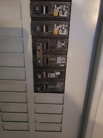 Close-Up Of A Circuit Breaker Panel With Six Switches Labeled With Different Amperages, Expertly Mounted In A Gray Metal Enclosure, Ideal For Running Power To A Grand Rapids Garage.