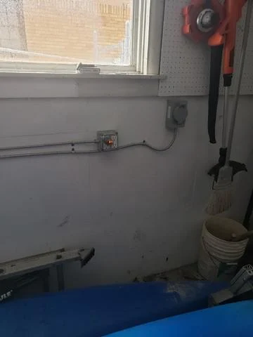 A Grand Rapids Garage Corner Features A Window, Electrical Outlets Perfect For Running Power, And Walls Adorned With A Hanging Broom, Buckets, And A Garden Tool.