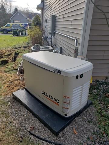 Generac Generator Installation Features An Outdoor Unit Placed On A Concrete Pad Beside The House, With Visible Utility Connections And A Lush Grassy Lawn In The Backdrop.