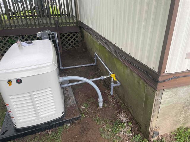 A White Generac Generator, Installed Next To The Exterior Of A Building, Provides Backup Power. Several Pipes Connect Seamlessly Between The Generator And The Building.